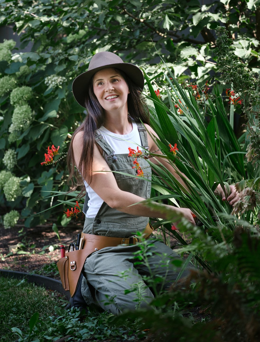 Gardener smiles while tending to plants in a sunny garden.