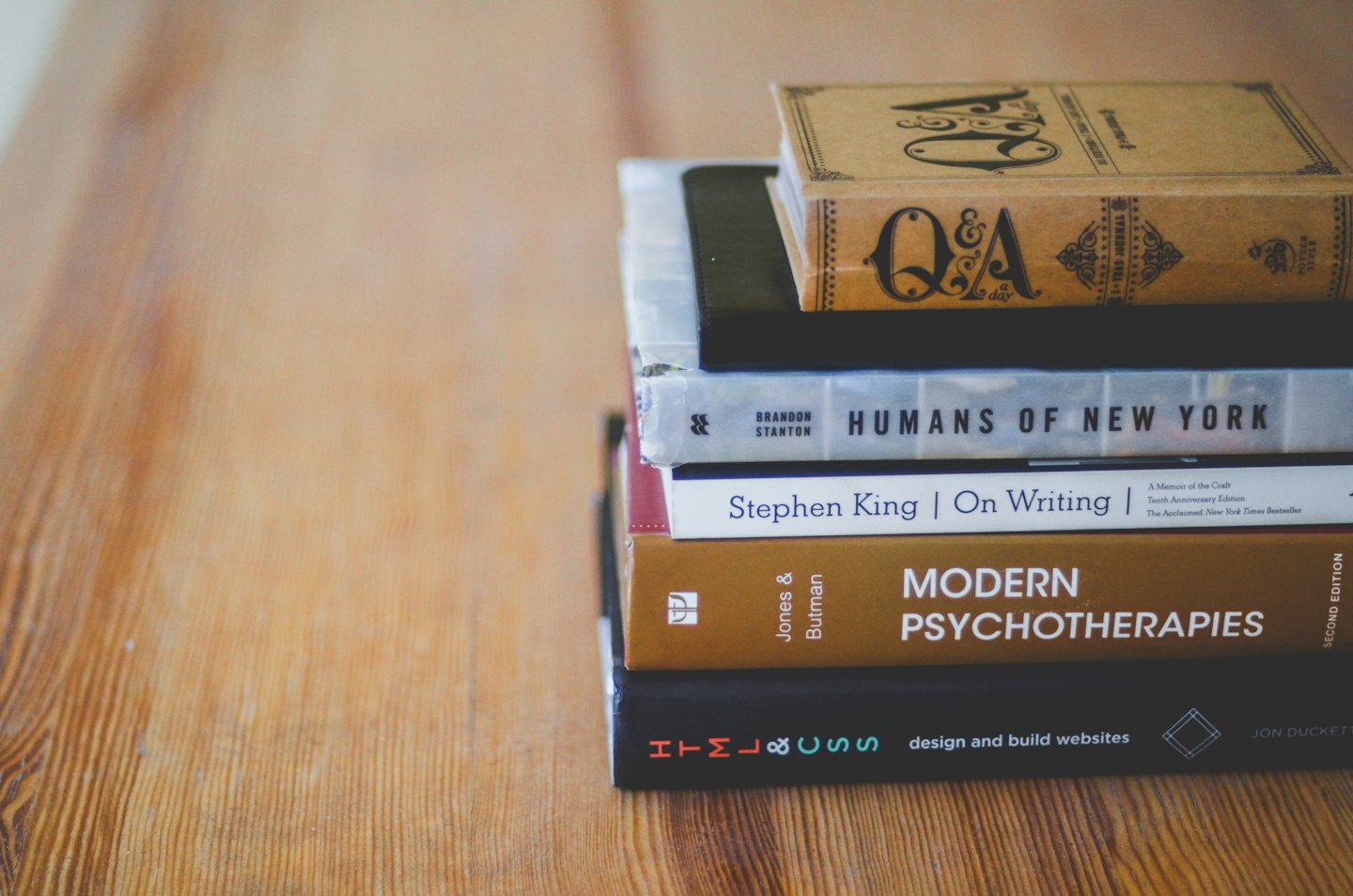 Five stacked books on a wooden table.