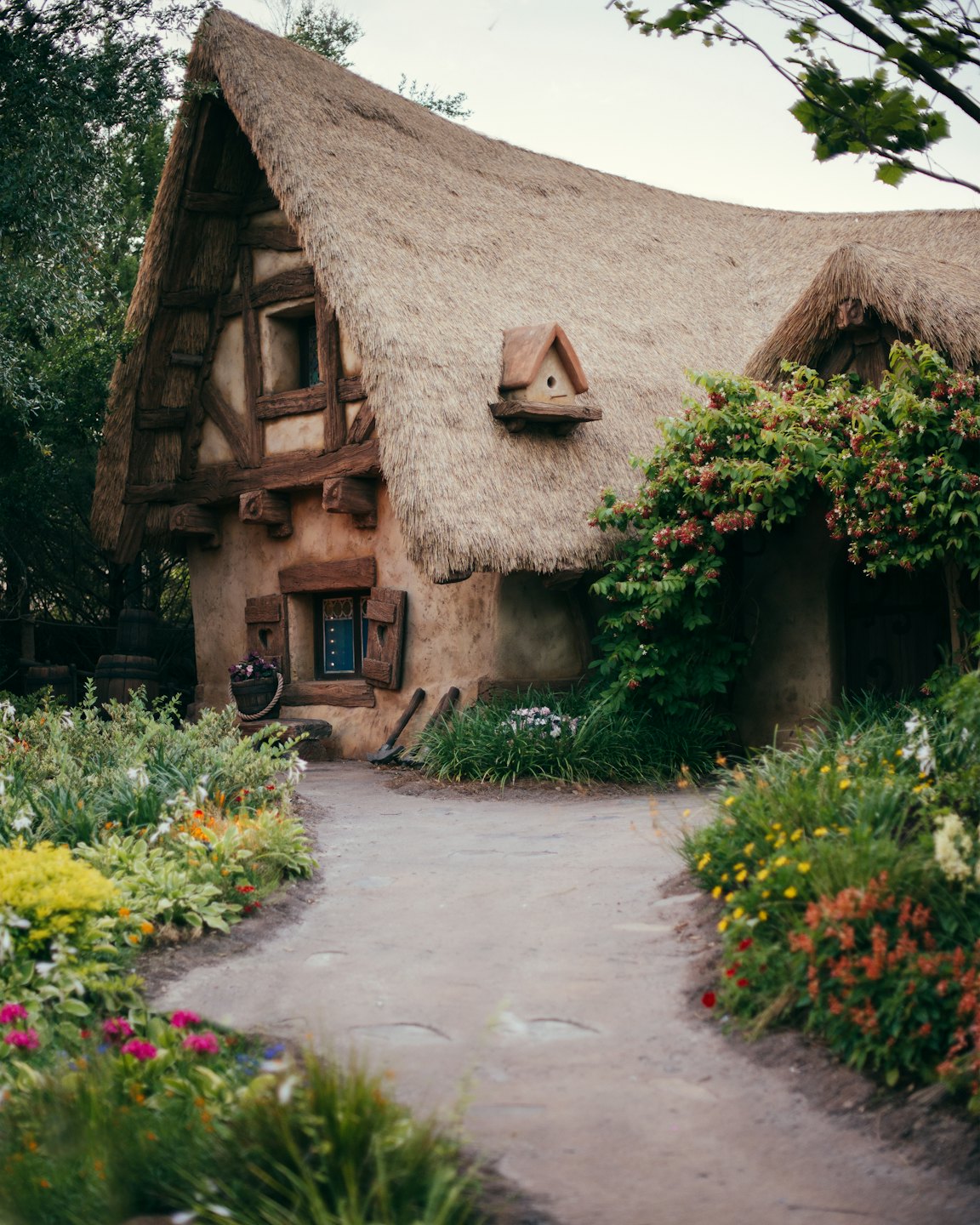 Fairytale cottage with thatched roof and flower-filled garden.