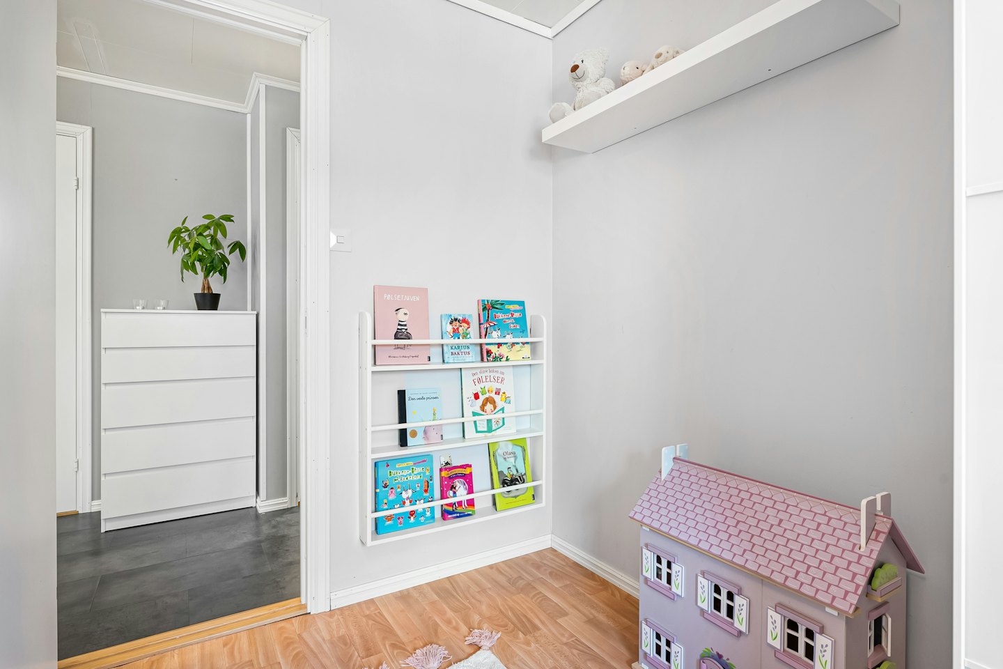 Childrens room with books, a purple dollhouse, and plush toys.